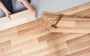 Installing laminated floor, detail on man hands holding wooden tile, over white foam base layer