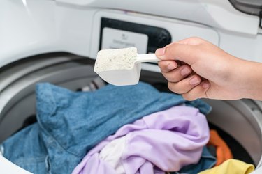Cropped Image Of Hand Holding Detergent Over Washing Machine