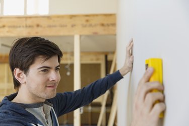 Young man with stud finder examining wall at home
