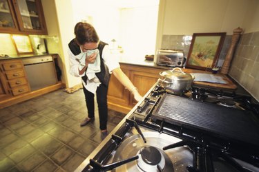 Woman in kitchen, turning off gas cooker, towel to face