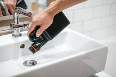 Removal of blockage in the sink, the hand of a man with a bottle of a special remedy with granules.