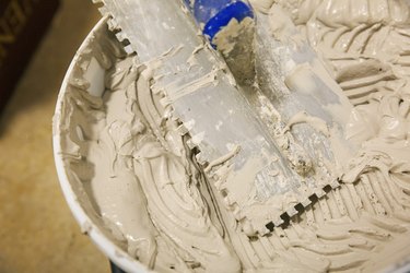Close up of a tiling trowel and bucket of tile adhesive.