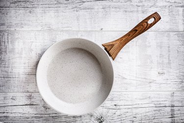 White frying pan on white rustic table.