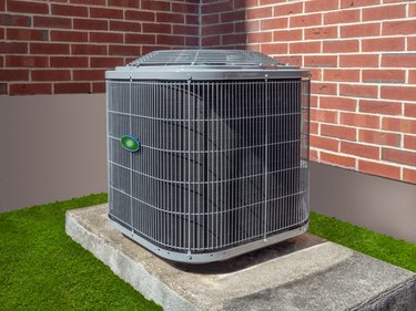 Air conditioning unit on concrete pad in yard next to brick wall