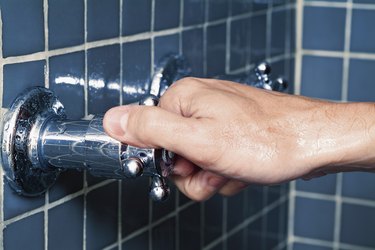 Hand turning water faucet in shower, close-up