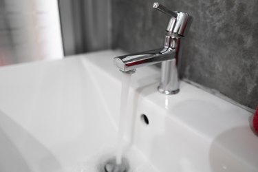 Running water from modern stainless steel faucet in white sink. Counter bathroom interior contemporary. Luxury and stylish design bathroom with a concrete style walls.