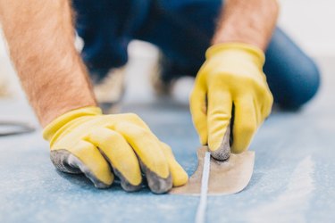 A master for laying linoleum using a month-old knife cuts off the excess welding cord after a hot spike of linoleum