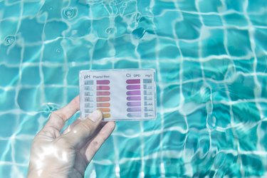 Girl's hand holding check kit dipping in to swimming pool water to test chlorine and pH