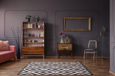 Vintage living room interior with a patterned rug, cupboard, golden frame on the wall, chair and wall molding