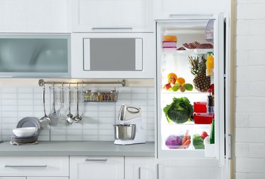 Open refrigerator full of products in stylish kitchen interior
