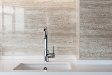 Detail of a white rectangular designer kitchen sink with chrome water tap against a tiled wall