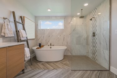 Freestanding bathtub sits right next to open shower and beautiful chevron patterned flooring