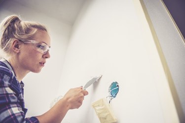 Young woman renovating her home, using wall repair kit and putty knife