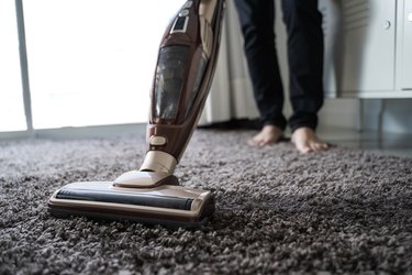 Low Section Of Man Cleaning Carpet With Vacuum Cleaner At Home