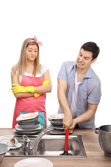 Young woman looking a young man trying to unclog sink