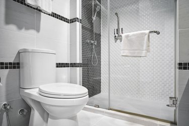 Shower and toilet in modern white bathroom with black tile accents.