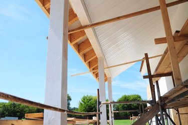 Building house patio roofing with wooden pillars and unfinished soffits and fascia boards installation.