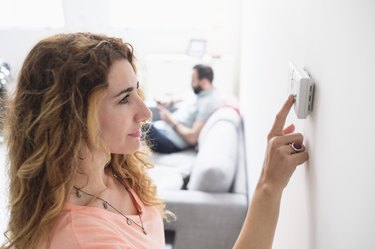 Mid-adult woman adjusting thermostat