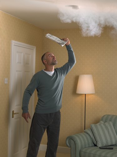 Man fanning smoke detector with newspaper