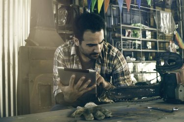 Man referencing chainsaw repair instructions on digital tablet