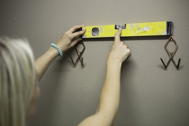 Blonde woman measuring with water level to fix coat hooks