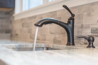 Closeup of water running from faucet in home kitchen or bathroom.