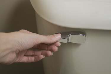 Close-up view of hand about to flush handle of tan toilet