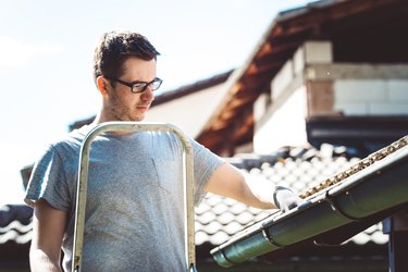 Man clearing leaves from gutter up high on ladder