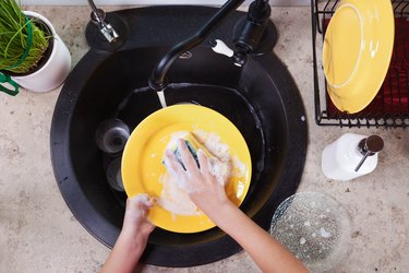 Child hands washing yellow plates at the kitchen sink