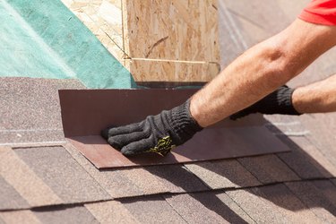 Roofer builder worker installing shingles on a new wooden roof