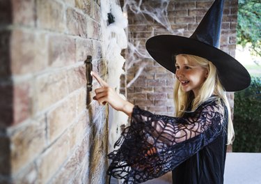 Girl dressed in witch costumes ringing door bell.