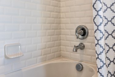 Closeup of modern white shower bath tub with blue curtains in bathroom in model home, apartment or house, tiles, faucet