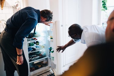 Mature male friends looking into refrigerator at kitchen