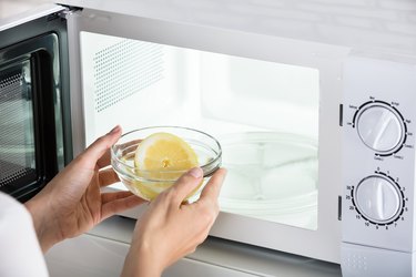 Woman Putting Bowl Of Slice Lemon In Microwave Oven