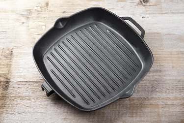 New empty cast aluminum grill pan with two handles on a wooden background.