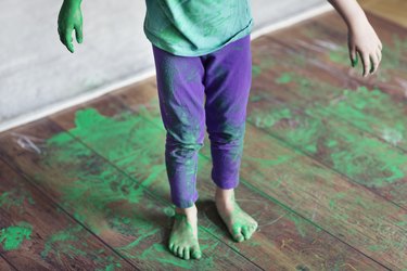 Spilled green paint on a child and wooden floor