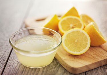 Small glass bowl of lemon juice with several lemon halves