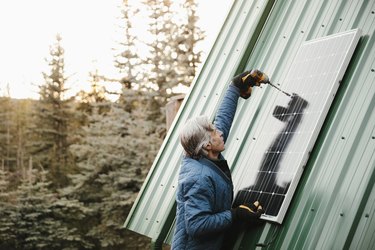 Man installing solar panel on cabin roof.