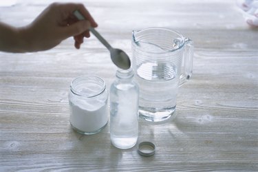 Adding powdered borax to bottle of water, using spoon, close-up