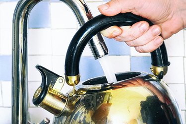Pours water into a kettle from a tap
