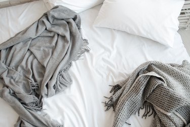 Unmade bed with pillow and gray blankets top view