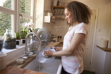 Woman Standing At Kitchen Sink Washing Up