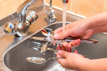Female hands washing cutlery under running water in the kitchen, hands close up
