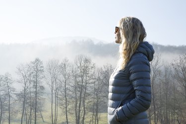 Woman walks through hilly meadow in mist