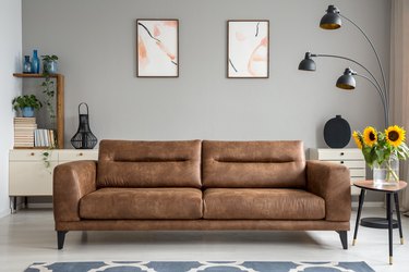 Leather sofa next to table with sunflowers in grey living room interior with posters. Real photo