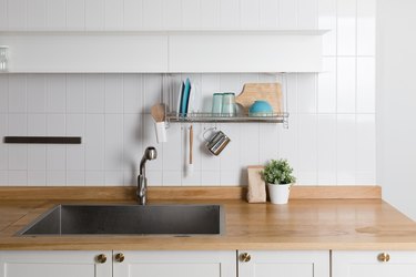 Clean dishes drying on metal dish rack on light background. Kitchen utensils and dishware on wooden shelf. Kitchen interior background.Text space.