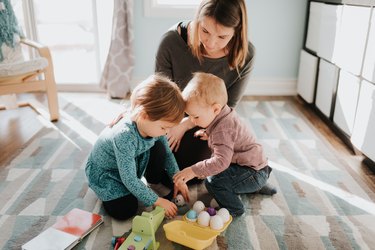 Female toddler playing with mother and baby brother in living room