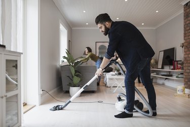 Man vacuuming floor while woman working in living room at home