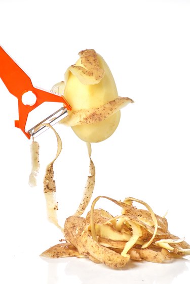 Peeler cleans potatoes, potato skin and peeled potatoes on a white background close-up