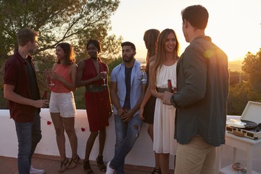 Young adult friends talk at a party on a rooftop at sunset